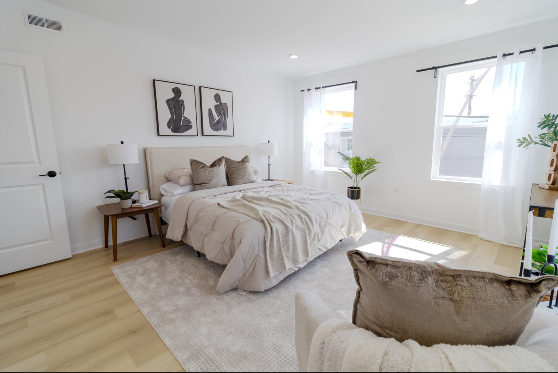 Sunlit primary bedroom with light wood floors and neutral furnishings