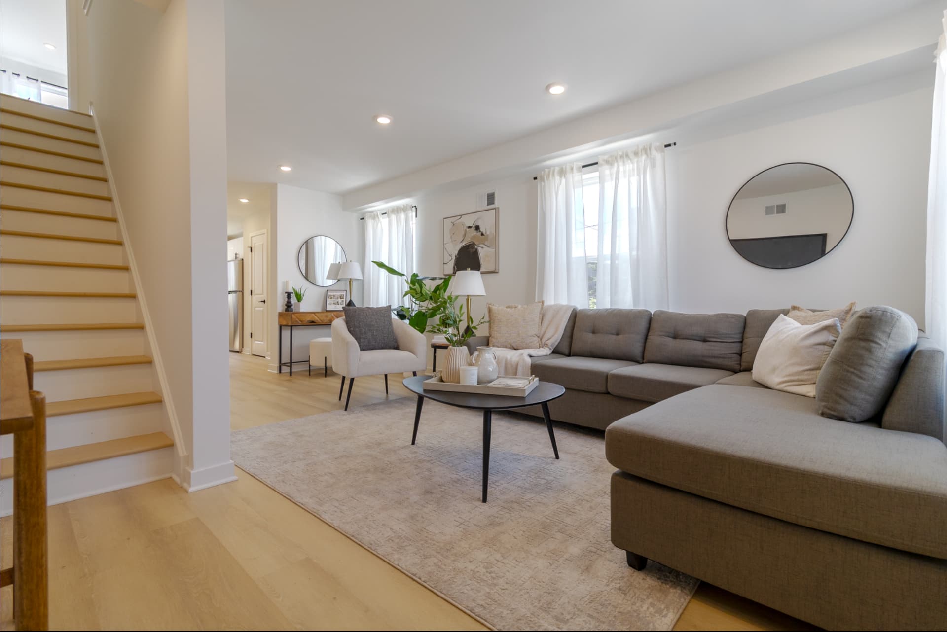 Open living room with sectional sofa, light wood floors, and staircase